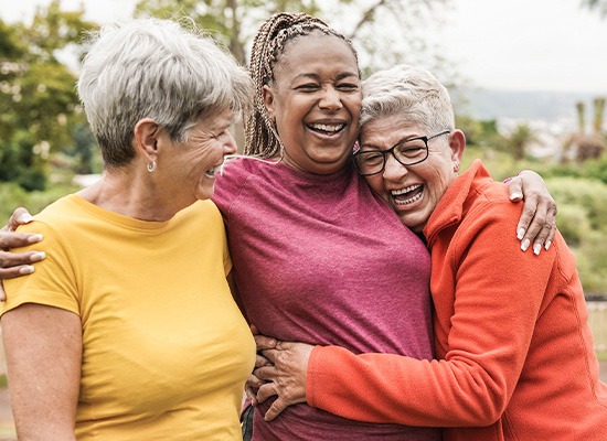 Three women in brightly colored shirts outside hugging