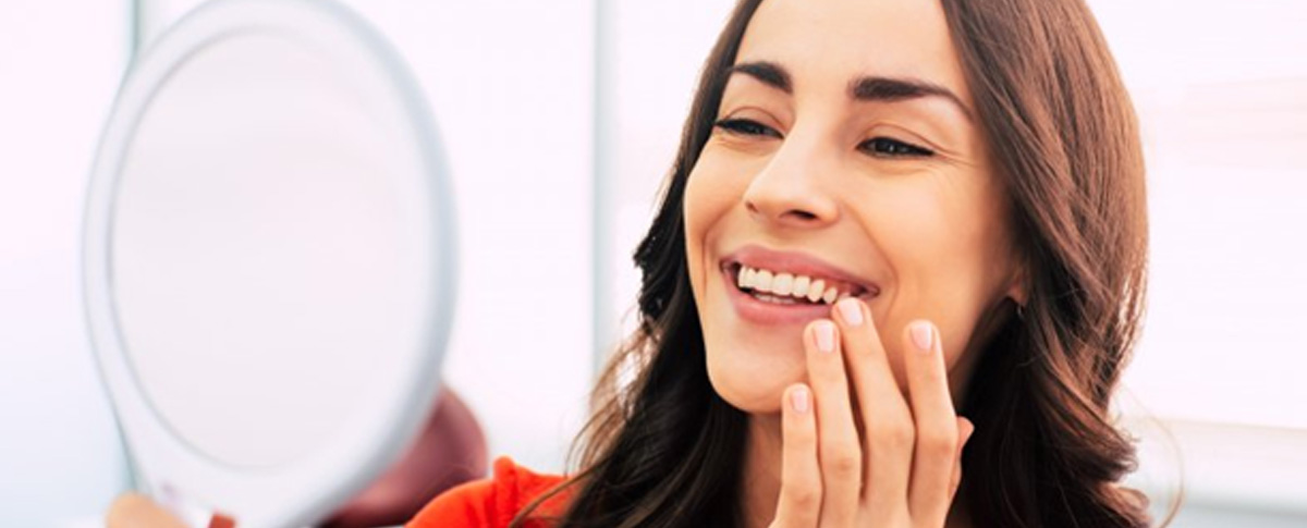 Woman touching her smile while looking at a small mirror